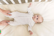 Baby in crib laying face up on organic cotton crib sheets in natural color.