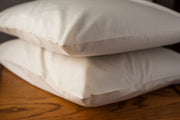 Organic cotton pillowcases in natural color with pillows stacked on a nightstand.