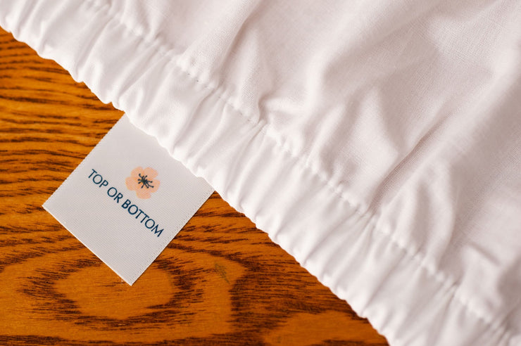 Organic cotton crib sheets in white color showing american blossom linens tag.